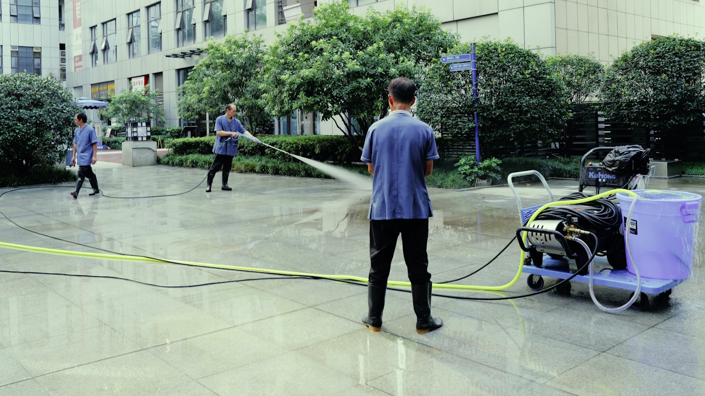 Maintenance workers clean a modern office plaza with power washers.